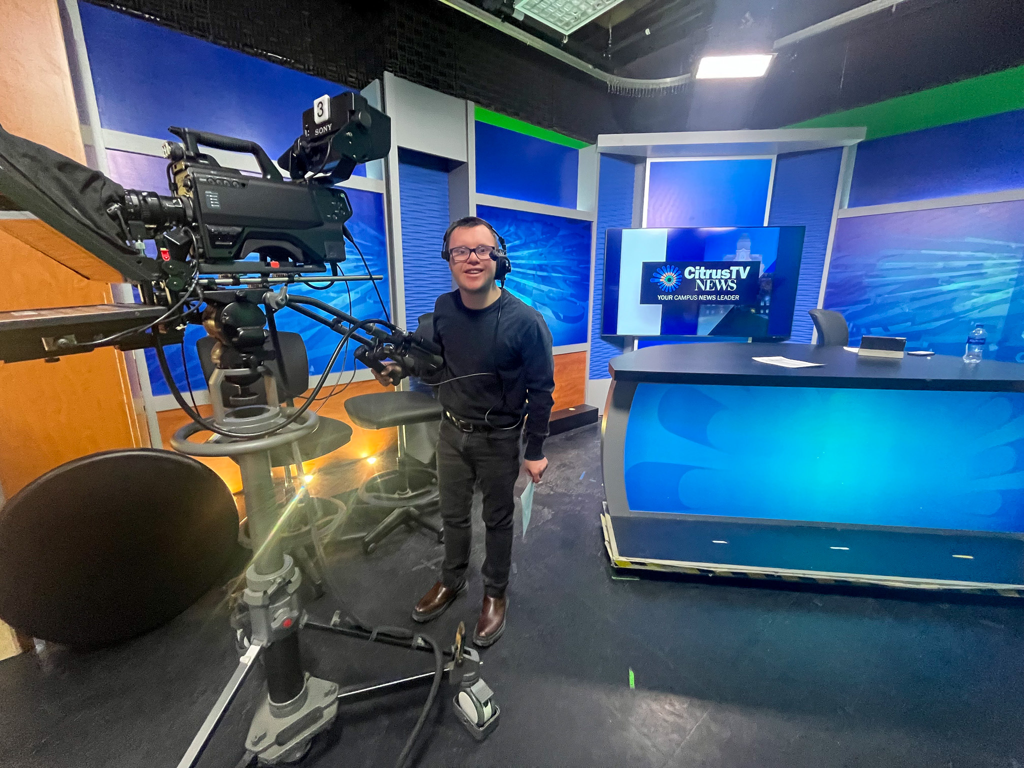 InclusiveU Student, Matthew Falanga, behind a camera with headphones on in a news studio.